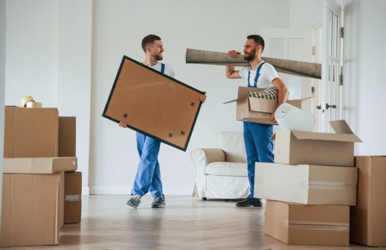 Painting and mat in hands. Two moving service employees in a room.